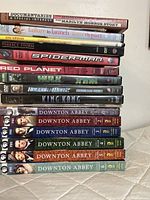 Photo showing a stacked assortment of DVDs including Downton Abbey season 1-6, Spider-Man, King Kong, Hulk, Hollow Man 2, Red Planet, Perfect Storm, Failure to Launch, and a Marilyn Monroe Story documentary.