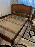 Full view of wooden double bed frame with headboard in a room, showing the side rails and support slats.