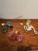 Photo showing all three collectible dragons placed on a wooden surface, each with distinctive colors and attached tags.