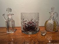 Front view of the 3-piece crystal set on wooden surface, showing crystal bowl and two decanters with one stopper placed separately.