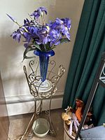 Full view of the glass vase, metal stand, and silk flowers from a side angle showing entire setup.