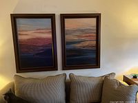 Both framed abstract landscape paintings mounted on wall above a couch, showing color palette and framing details.