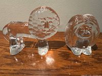 Front view showing both lion and troll sculptures together on a wooden surface, highlighting the clear glass and textured abstract features.