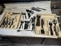 Wide view of entire cutlery set showing multiple forks, knives, teaspoons, tablespoons, and one beige storage tray on a countertop.
