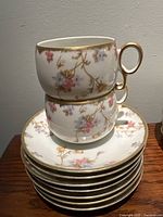 Stacked tea cups and saucers showing floral pattern in pink and blue with gold rim