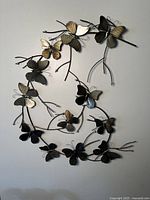 Photo showing metal butterfly wall art mounted on wall, featuring numerous butterflies on curved branches.
