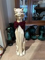Front view of the white ceramic cat sculpture sitting upright with a red velvet bow tie and modern abstract geometric design.