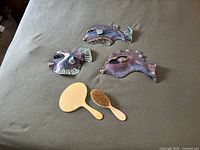 Three multicolored ceramic fish wall art pieces paired with a French ivory vanity set including a hand mirror and hairbrush laid out on fabric.