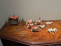 Full view of the miniature Queen Elizabeth II Coronation Coach, six horses with riders and the Lady & The Tramp miniature figurines laid out on a wooden surface.