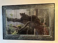 Framed print of a black panther resting on a branch in a forest, showing the detailed wood frame and protective glass.