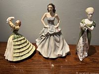 Front view of three porcelain Royal Doulton figurines grouped together showing detailed dresses and postures.