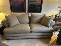 Front-facing photo of a beige fabric sofa with three large back cushions and two smaller pillows in a traditional design, showing the full sofa from front.