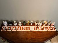 Full set of 12 miniature porcelain vases displayed with corresponding design cards on a wooden surface.
