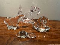 Four clear glass animal figurines placed together: squirrel nut dish, polar bear, snail, and beaver, displayed on a wooden surface against a white wall.