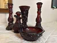 Full set of cranberry pressed glass pieces shown together on white surface