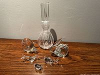 Photo showing the decanter with vertical grooves and six small glass animal figurines including rabbit, pig, seal, whale, bird, and fish arranged in front of a plain wall.