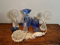 Full lot arrangement showing 2 pressed glass perfume bottles with fish stoppers, matching trinket container, 3 blue crystal bottles with faceted stoppers including one with atomizer, and a small clear bottle