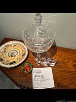 Photo of the full lot including the pressed glass candy dish with lid, the Native American plate with central chief image, glass hippo figurine, and a decorative round glass paperweight.