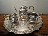 Silver plated teapot, sugar bowl, creamer shown on ornate Chippendale style serving tray, all with detailed ornate patterns and polished finish.