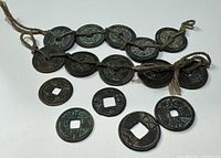 Photo showing several vintage Chinese Feng Shui coins including some strung on natural fiber string with detailed Chinese characters.