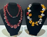 Two necklaces on black bust display: one red faceted lucite bead necklace with rhinestone ball centerpiece and one multicolored irregular lucite bead necklace.