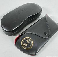 Photo of two Ray-Ban sunglasses cases, one soft black leather-like with red interior and gold logo sticker, one black hard case embossed with logo
