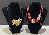 Front view of both necklaces on black necklace display busts, showing bead details and cords.