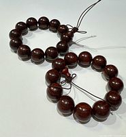 Two rosewood Tibetan Buddhist prayer bracelets with different bead sizes, displayed on white background at an angle showing bead shine and string knots.