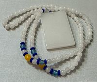 Photo of the necklace showing the rectangular white jade pendant and the beaded chain with blue and yellow accent beads.