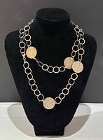 Necklace shown on black stand, front view, highlighting linked oval rings and round coin charms in gold-tone metal.