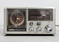 Front view of the YORX AM/FM Quartz Clock Radio showing analog clock face on left and radio dial on right, including knobs and switches for alarm, tone, volume, and tuning.