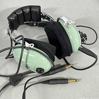 Close-up image of David Clark H10-60 headset showing the light green ear cups, black foam ear cushions, padded leather headband, attached cables with dual plugs.