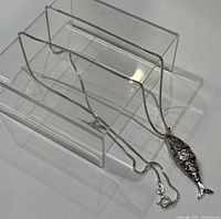 Full view of silver fish pendant necklace with chain displayed on clear acrylic stand