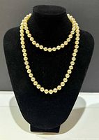 Long vintage pearl necklace displayed on black velvet stand showing full length and pearl consistency.