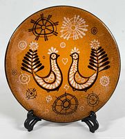 Front view of the pottery wall plate showing stylized birds, floral and abstract motifs in black and white on an orange-brown background.