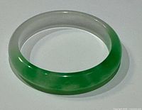 Top view of the natural Asian green and white jade D shaped bangle laid flat on white background showing the coloration and shape.