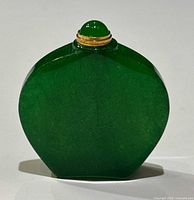 Front view of the green jade bottle showing the flat, rounded shape and gold accented rounded stopper.