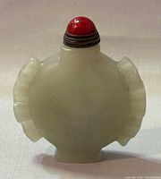 Front view showing rounded flat bottle body with carved side extensions and red capped lid.