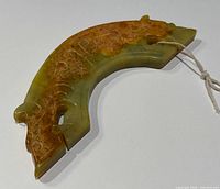 Front angled view of curved jade double dragon carving showing detailed etched patterns and coloration.