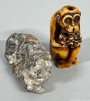 Two carved figurines shown together. The first is a hand carved Japanese netsuke monkey, with a hole on top and holding smaller monkeys. The second is a carved stone animal figurine resembling a big cat in a lying position. Photo shows front and side view.