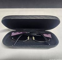Opened black textured sunglasses case holding PRADA sunglasses inside.