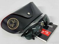 Photo of Ray-Ban sunglasses, black leather case with gold logo, and Ray-Ban booklet on white background.