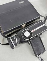 Eumig Viennette 5 Super 8 movie camera body with visible dial and lens markings, placed beside or on the carrying case.