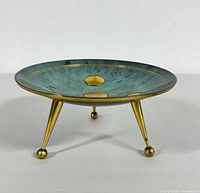 Front angle showing the brass legs and teal enamel interior with brass details of the shallow bowl.