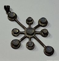 Front view of silver pendant featuring central round moonstone and eight surrounding smaller moonstones, set in silver bezels with radial connecting arms.