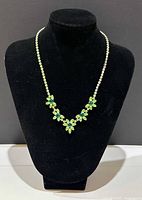 Vintage Signed Sherman necklace with five green rhinestone flower clusters displayed on black velvet bust, front view.
