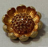 Close-up top view of vintage floral brooch showing detailed gold-tone petals and center with amber rhinestones.