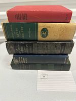 Stack of five hardcover books with different colored bindings showing spines and partial top edges, placed on a white surface.