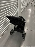 Rear side view of the black Britax B-Lively stroller showing the handlebar, storage basket, and wheels.