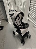 Front angled view of lightweight single Graco stroller, showing parent tray with cup holders, child tray, light gray seat fabric, and folding canopy.